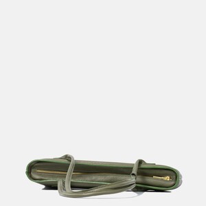May include: A sage green leather tote bag with a textured surface, featuring a gold-toned metal zipper closure along the top edge. The bag includes two matching leather shoulder straps and is finished with a contrasting darker green edge trim.