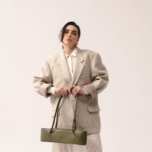 May include: An olive green rectangular shoulder bag with thin straps, worn with an oversized beige speckled blazer, a white collared shirt, and a white lace skirt. The bag features a structured, elongated horizontal shape and a smooth finish.