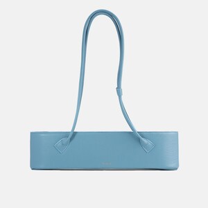 May include: A light blue, horizontally elongated rectangular handbag with a textured surface. It features a single, long, thin shoulder strap attached to the top corners of the bag. The design is minimalist with a small, centered logo on the front.