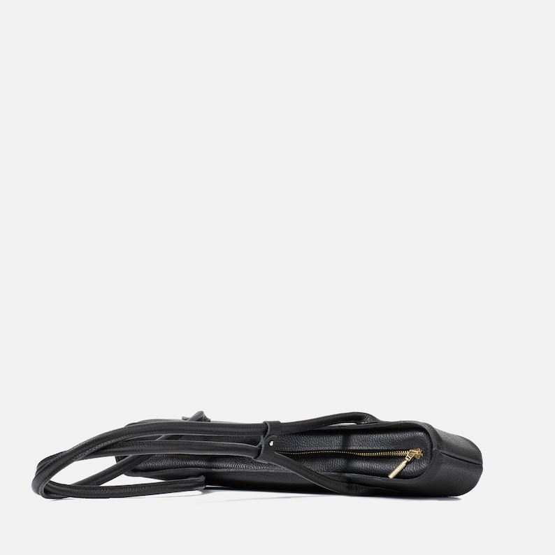 May include: A black pebbled leather tote bag laid horizontally, featuring a top zipper closure with a gold-toned metal pull, two long shoulder straps, and a structured rectangular base with visible stitching along the edges.