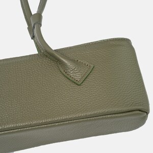 May include: An olive green handbag featuring a textured, pebbled surface. The bag includes a sturdy handle attached with triangular stitching details. The design showcases a clean, rectangular base structure with visible seams along the edges.