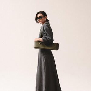May include: A long-sleeved charcoal gray maxi dress with a collared neckline and a full-length skirt, paired with a structured olive green rectangular shoulder bag featuring dual top handles and a smooth, matte finish.