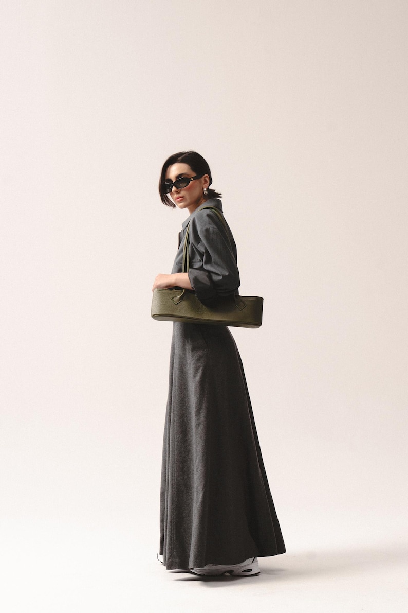 May include: A long-sleeved charcoal gray maxi dress with a collared neckline and a full-length skirt, paired with a structured olive green rectangular shoulder bag featuring dual top handles and a smooth, matte finish.