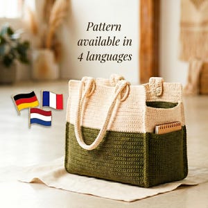 Könnte beinhalten: Eine zweifarbige Häkeltasche mit einem cremefarbenen oberen Teil und einem dunkelolivgrünen unteren Teil, ausgestattet mit zwei Henkeln und einer Seitentasche mit einem kleinen Notizbuch. Text: Pattern available in 4 languages.