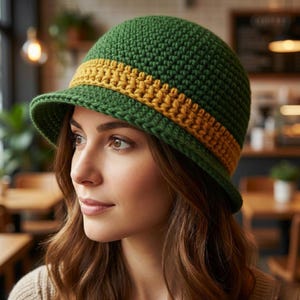 May include: A green crochet cloche hat with a mustard yellow band. The hat has a small brim and a rounded crown. The hat is made of a textured yarn and is a stylish accessory.