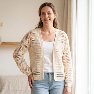May include: A cream-colored open-front cardigan featuring a crochet mesh stitch pattern throughout the body and sleeves, with solid ribbed trim along the front edges, cuffs, and hem, worn over a plain white top and light blue denim jeans.