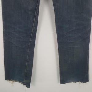 May include: Dark wash denim jeans with a raw, frayed hem. The jeans have a straight leg cut and show signs of wear. The fabric is a deep indigo blue with subtle fading. The jeans are a classic style.