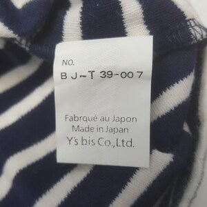 May include: Close-up of a white tag with black text, attached to a navy blue and white striped fabric. The tag reads "NO. BJ-T 39-007", "Fabriqu&eacute; au Japon", "Made in Japan", and "Y's bis Co., Ltd."
