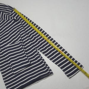 May include: Navy blue and white striped long-sleeve shirt. A yellow measuring tape is laid across the sleeve, showing a length of approximately 22 inches. The shirt has a classic nautical design.