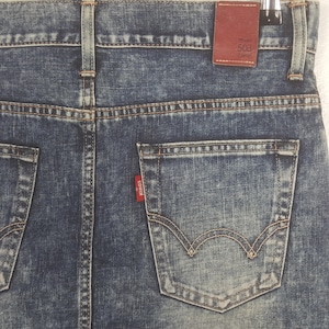 Puede incluir: Primer plano de la parte trasera de unos vaqueros azules. Los vaqueros tienen un lavado descolorido y costuras visibles. Una peque&ntilde;a etiqueta roja con la marca "EDWIN" est&aacute; en el bolsillo trasero. Una etiqueta de cuero marr&oacute;n con "Model 503" es visible.