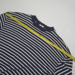 May include: Navy blue and white striped long-sleeve shirt. The shirt is measured with a yellow tape measure. The shirt has a crew neck and a tag on the back of the neck. The stripes are horizontal and evenly spaced.