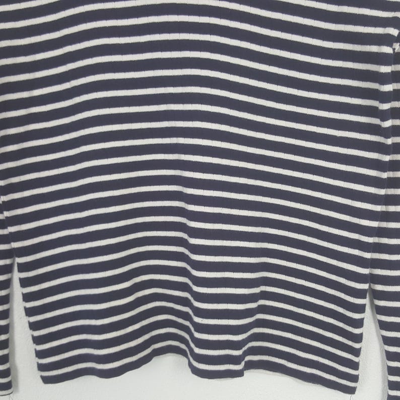May include: Close-up of a navy blue and white striped long-sleeve shirt. The shirt features horizontal stripes in a classic nautical design. The sleeves are visible on either side of the frame, and the fabric appears to be a soft knit.