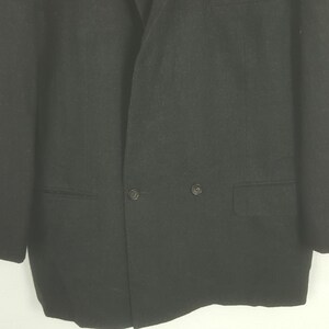 May include: A close-up shot of a black blazer. The blazer has a double-breasted design with two rows of buttons and two front pockets. The fabric appears to be a solid, dark color.