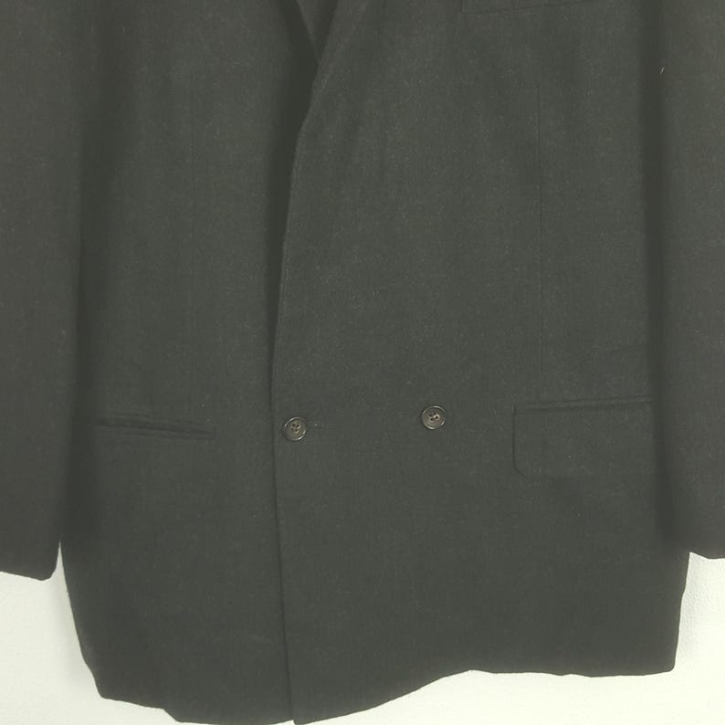 May include: A close-up shot of a black blazer. The blazer has a double-breasted design with two rows of buttons and two front pockets. The fabric appears to be a solid, dark color.