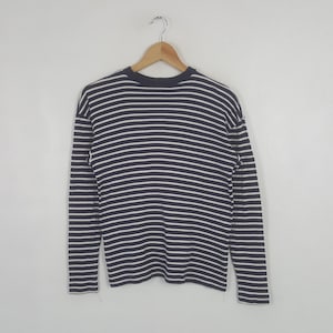 May include: A long-sleeved shirt with horizontal navy blue and white stripes. The shirt is hanging on a wooden hanger against a plain white background. The shirt's design is a classic nautical style.