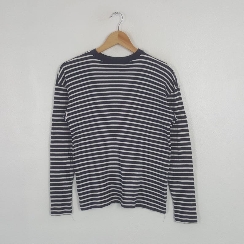 May include: A long-sleeved shirt with horizontal navy blue and white stripes. The shirt is hanging on a wooden hanger against a plain white background. The shirt's design is a classic nautical style.