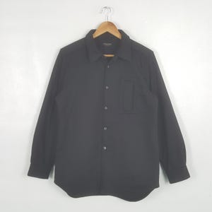 May include: A white ceramic mug with a black handle and the text "But First, Coffee" in a black, handwritten-style font. The mug is on a white surface.