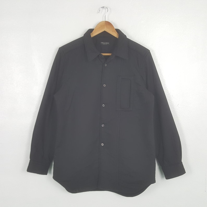 May include: A white ceramic mug with a black handle and the text "But First, Coffee" in a black, handwritten-style font. The mug is on a white surface.