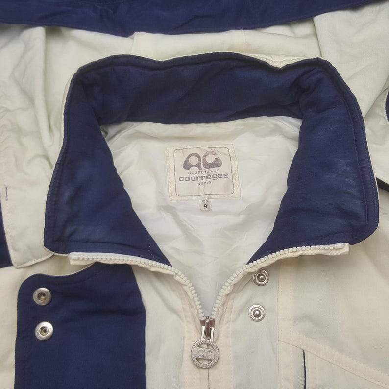 Pode incluir: Casaco creme com detalhes em azul marinho. O casaco tem fecho de correr, bot&otilde;es de press&atilde;o e gola. O log&oacute;tipo da marca "courr&egrave;ges paris" &eacute; vis&iacute;vel numa etiqueta dentro da gola. Tamanho 9.
