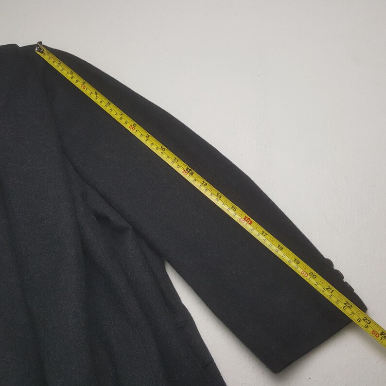 May include: A dark gray blazer with a yellow measuring tape laid across the sleeve. The tape shows measurements in inches. The blazer has a classic design with buttons on the cuff.
