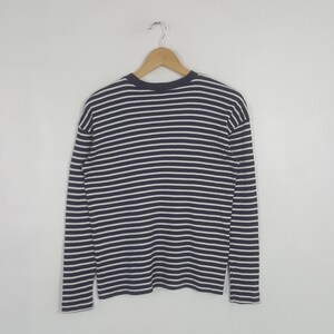 May include: A navy blue and white striped long-sleeve shirt hanging on a wooden hanger. The shirt features horizontal stripes and a crew neck design. The garment is made of a soft, comfortable material.