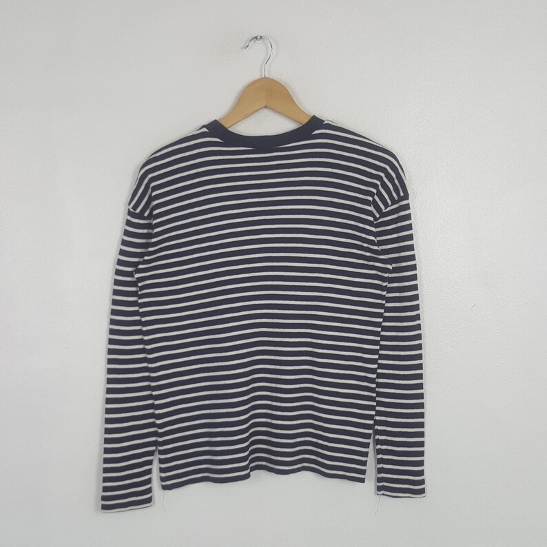 May include: A navy blue and white striped long-sleeve shirt hanging on a wooden hanger. The shirt features horizontal stripes and a crew neck design. The garment is made of a soft, comfortable material.