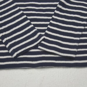 May include: Close-up of a navy blue and white striped long-sleeve shirt. The shirt's sleeves are visible, with the stripes running horizontally. The fabric appears to be a soft knit material, suitable for casual wear.