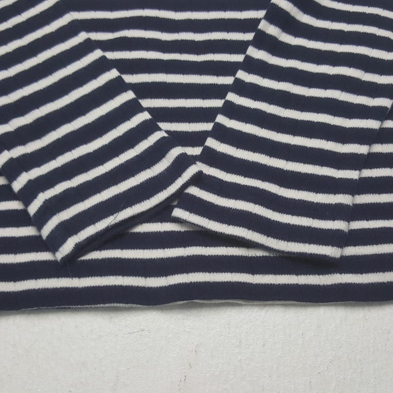May include: Close-up of a navy blue and white striped long-sleeve shirt. The shirt's sleeves are visible, with the stripes running horizontally. The fabric appears to be a soft knit material, suitable for casual wear.