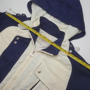 Pode incluir: Casaco creme com detalhes em azul marinho, capuz e fecho de correr. O casaco tem fechos de press&atilde;o e um cord&atilde;o. O casaco tem aproximadamente 51 cm de comprimento.