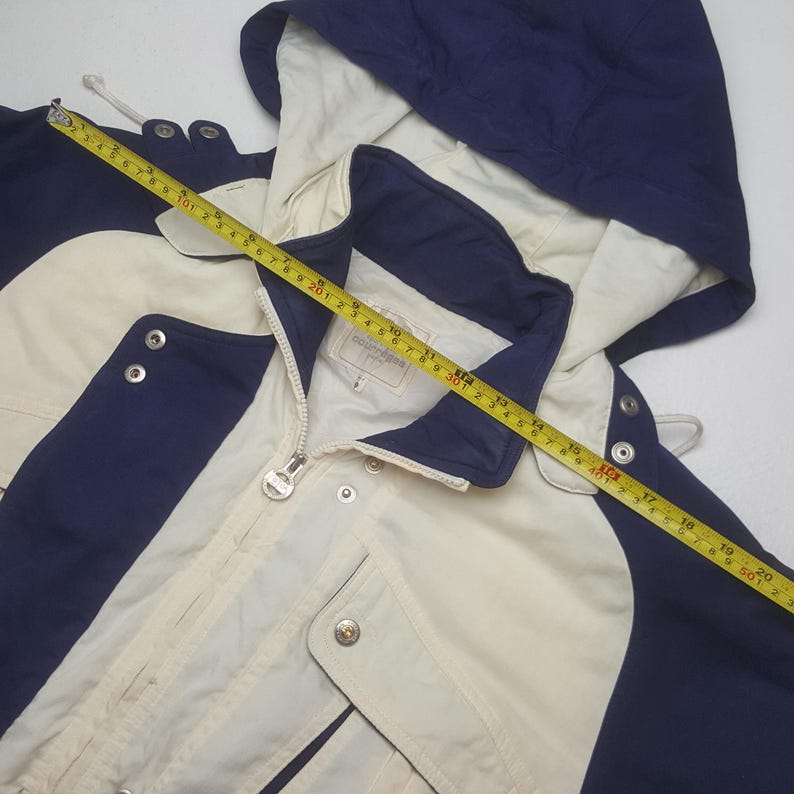 Pode incluir: Casaco creme com detalhes em azul marinho, capuz e fecho de correr. O casaco tem fechos de press&atilde;o e um cord&atilde;o. O casaco tem aproximadamente 51 cm de comprimento.