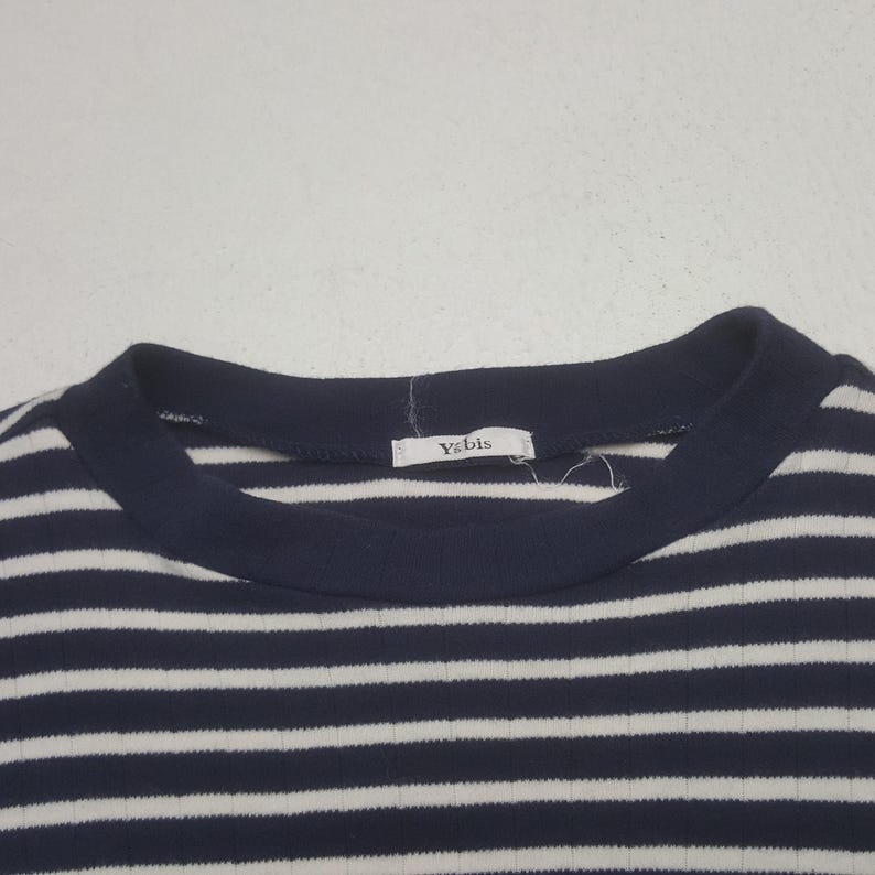 May include: Close-up of a navy blue and white striped ribbed knit top. The top features a crew neck and a tag that reads "Y's bis". The stripes are horizontal and evenly spaced.
