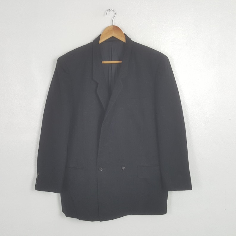 May include: A black blazer with a double-breasted design, hanging on a wooden hanger. The blazer has two rows of buttons and a notched lapel. The garment is made of a solid, dark fabric.