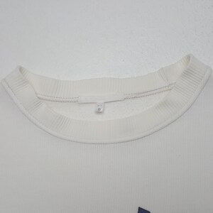 May include: A white crewneck sweatshirt featuring a ribbed collar and a small interior fabric tag at the neckline. The garment is made of a textured material and includes a white label with the number 9 printed in black on the inner collar.