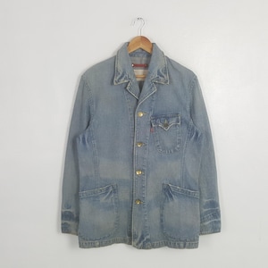 May include: Light blue denim jacket with a classic collar, gold buttons, and multiple pockets. The jacket has a vintage look, with a small red tag on the chest pocket. The jacket is hanging on a wooden hanger.