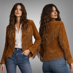 Peut inclure: Veste en daim marron avec des franges. La veste a des manches longues et un design sans col. Les franges sont le long des manches, du dos et du devant. Le modèle porte une chemise blanche et un jean bleu.