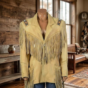 Puede incluir: Chaqueta de ante color canela con flecos largos. La chaqueta presenta costuras decorativas y patrones geométricos en los hombros. Tiene un estilo western clásico con solapas y bolsillos.