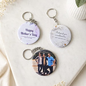 Könnte beinhalten: Drei runde Schlüsselanhänger. Zwei Schlüsselanhänger haben Blumendesigns und den Text "Happy Mother's Day" und "Thank you for your unconditional love." Der dritte Schlüsselanhänger zeigt ein Foto von drei Personen. Alle haben silberne Schlüsselringe.