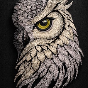 Puede incluir: Bordado detallado de la cabeza de un búho, con un llamativo ojo amarillo y detalles intrincados de plumas. La cara del búho está representada en tonos grises y crema sobre un fondo negro, creando un efecto texturizado y tridimensional.