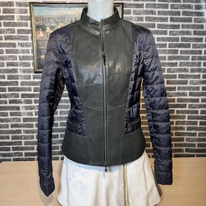 May include: A dark gray and navy blue jacket with a quilted design on the sleeves and sides. The front of the jacket is a darker gray leather with a full-length zipper. The jacket is displayed on a mannequin.
