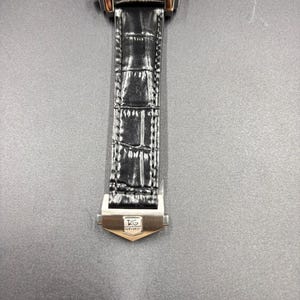 K&ouml;nnte beinhalten: Eine Armbanduhr mit quadratischem Geh&auml;use und leuchtend gr&uuml;nem Zifferblatt, das zwei schwarze Hilfszifferbl&auml;tter und wei&szlig;e Markierungen aufweist. Die Uhr hat ein poliertes silberfarbenes Metallgeh&auml;use und ein schwarzes strukturiertes Lederarmband mit einer silberfarbenen Metallschlie&szlig;e, die das TAG Heuer-Logo zeigt.