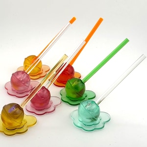 May include: A selection of colourful drink stirrers. Each stirrer has a spherical, translucent orb on a flower-shaped base. The stirrers are in various colours, including yellow, pink, orange, green, and clear, with matching or contrasting stems.