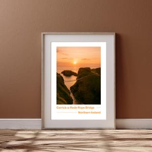 May include: Framed print of the Carrick-a-Rede Rope Bridge in Northern Ireland, depicting a sunset over the sea. The image shows a suspension bridge between cliffs, with the text "Carrick-a-Rede Rope Bridge - Northern Ireland".