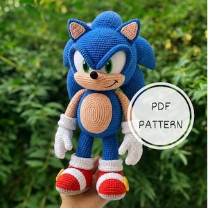 Könnte beinhalten: Ein gehäkeltes Plüschtier in Blau, Weiß und Beige, das einem Igel-Charakter ähnelt, mit großen weißen Augen, grünen Pupillen und roten Schuhen mit gelben Akzenten. Das Bild enthält eine weiße kreisförmige Grafik mit dem Text PDF PATTERN.