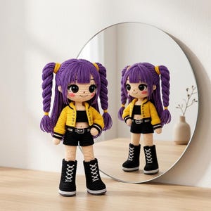 May include: A crocheted doll with purple pigtails, a yellow jacket, black top, shorts, and boots. The doll stands before a round mirror, its reflection visible. The doll has a smiling face. The doll is handmade.
