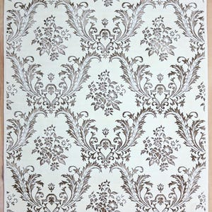 May include: Cream-colored rug with a repeating pattern of brown floral and leaf motifs. The design features stylized flowers and scrolling leaves, creating a classic, ornate look. The rug has a white fringe along the edge.