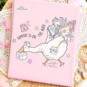 Puede incluir: Un cuaderno rosa claro con una oca de dibujos animados vestida de enfermera, cargando un kit médico y suministros como un estetoscopio, bolsa de sangre y vacuna. El texto dice SUPPORT IS ON THE WAY e incluye el logo de Lil Paw Digital.