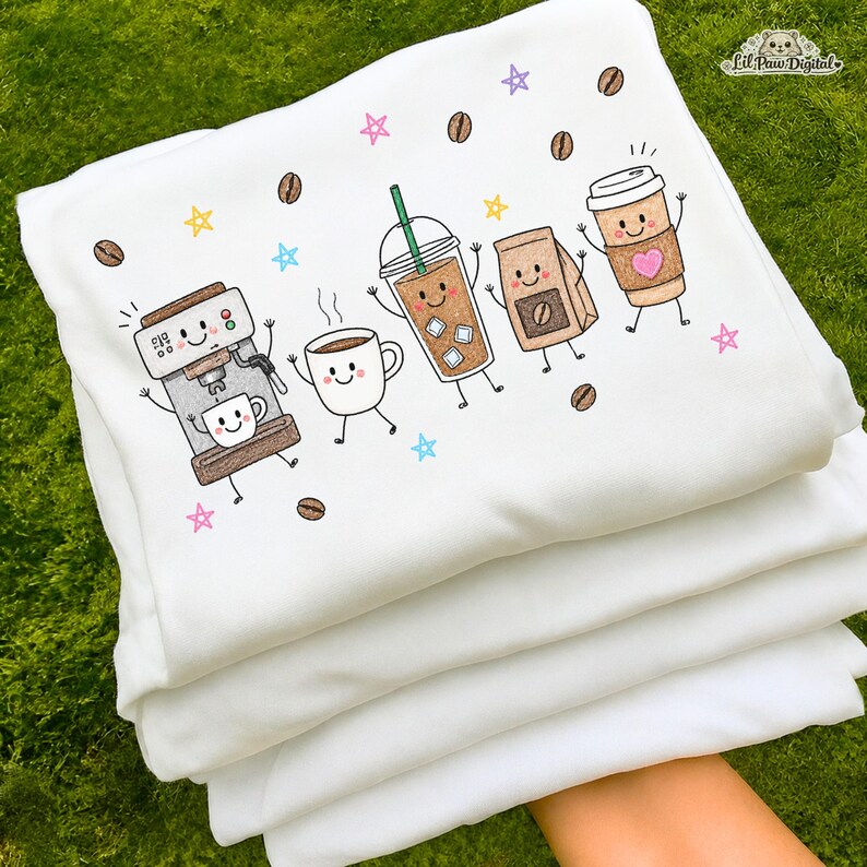 May include: A white sweatshirt featuring a colorful graphic print of anthropomorphic coffee items including an espresso machine, a mug, an iced coffee, a coffee bag, and a paper cup with a pink heart, surrounded by coffee beans and stars.
