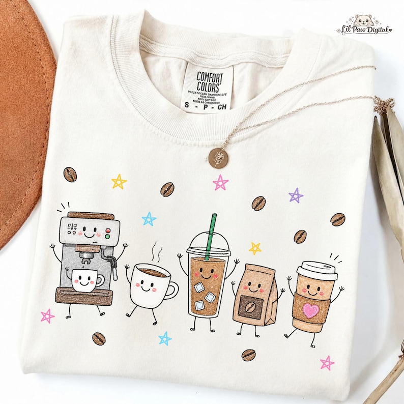 May include: A cream-colored t-shirt featuring a graphic print of five anthropomorphic coffee-themed characters, including an espresso machine, a mug, an iced coffee, a coffee bag, and a paper cup, surrounded by coffee beans and colorful stars.