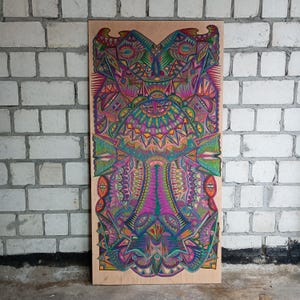 Puede incluir: Una obra de arte simétrica y vibrante sobre un panel de madera. La pieza presenta patrones y diseños intrincados en un caleidoscopio de colores, incluyendo rosa, verde, azul y amarillo. La obra de arte se exhibe contra una pared de ladrillos blancos.