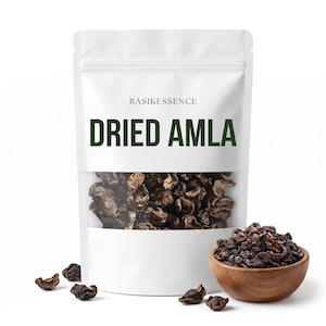 Może przedstawiać: Biała torebka stojąca z etykietą RASIKESSENCE DRIED AMLA i przezroczystym okienkiem ukazującym ciemnobrązowe kawałki suszonej amli. Po prawej stronie znajduje się drewniana miseczka z tymi samymi suszonymi owocami, a z przodu leżą luźne kawałki.